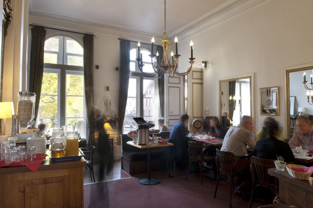 Een eethoek met een kroonluchter, grote ramen en uitzicht op buiten.