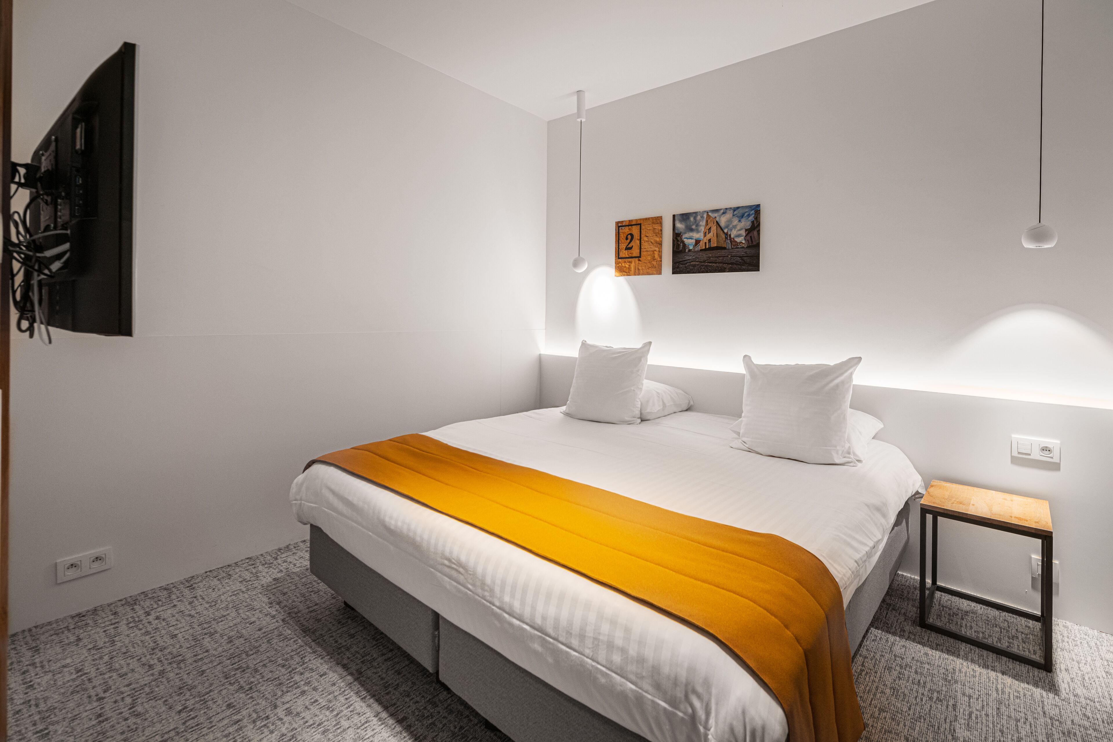 Una habitación de hotel moderna con una cama grande, una mesita de noche y un televisor montado en la pared.