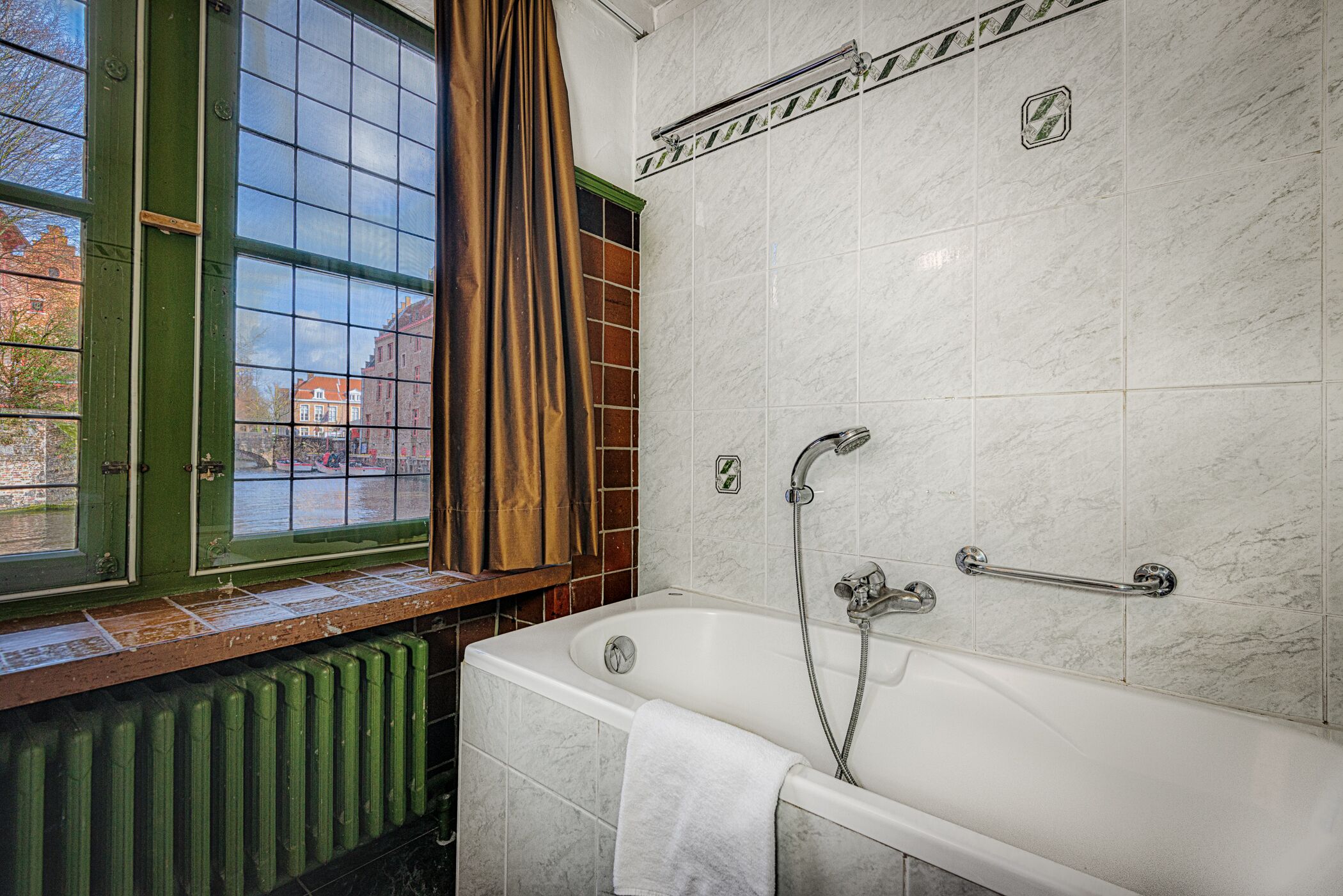 Une salle de bain avec une baignoire, une fenêtre donnant sur des immeubles et un radiateur.