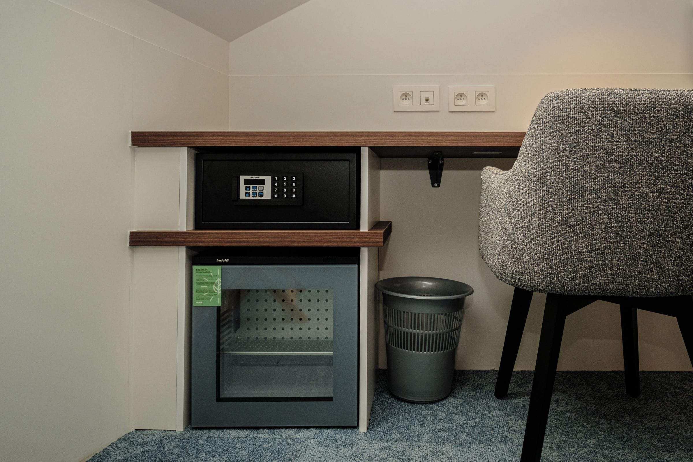 Une petite cuisine équipée, avec un four encastré, une poubelle et une chaise.