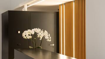 A modern reception desk with a dark finish, a vase with white flowers, and a wooden slat wall to the right.