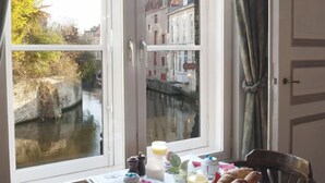 A dining table with breakfast items and a view of a canal and buildings.