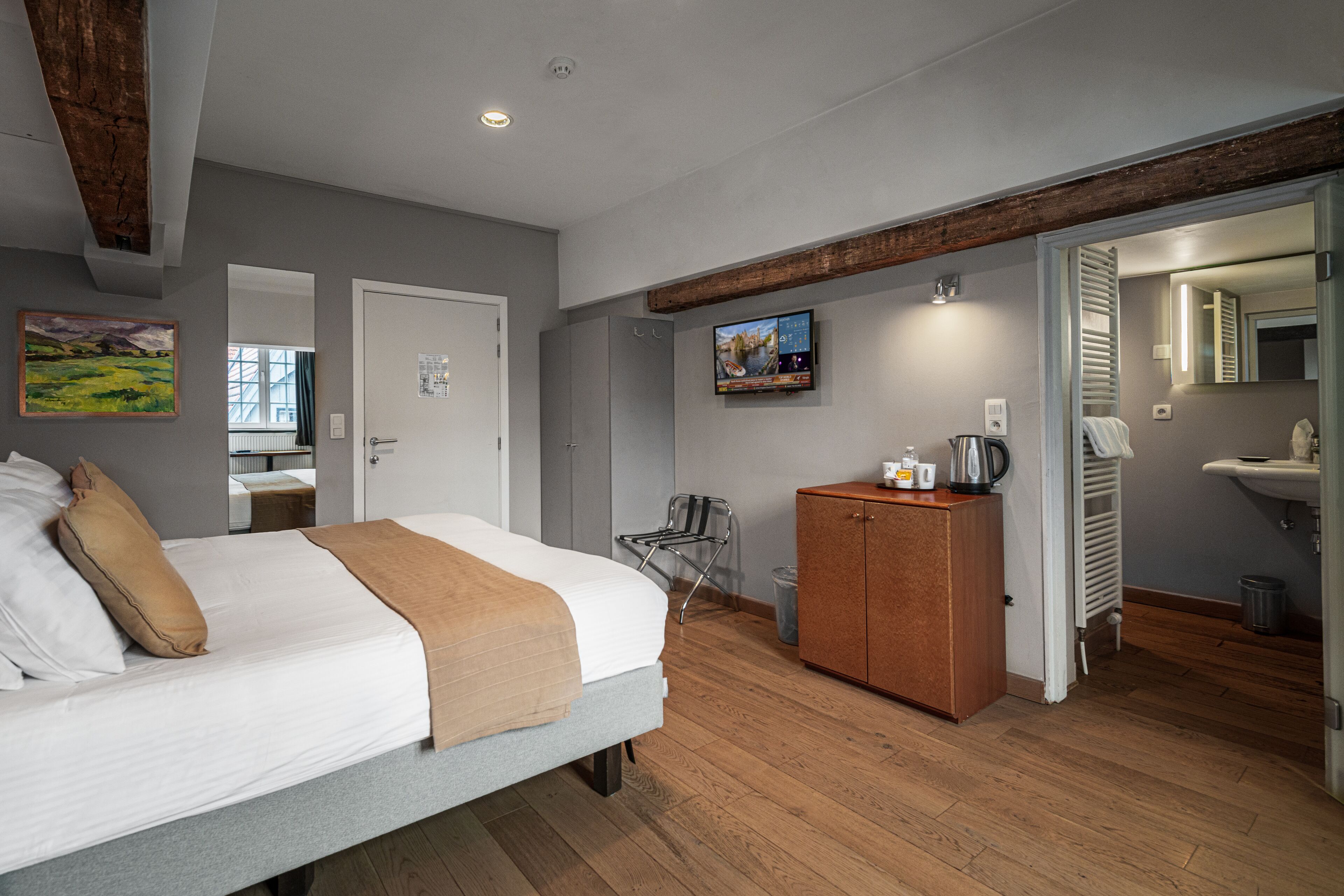A modern hotel room with a bed, a wooden cabinet, a television, and a bathroom visible through an open door.