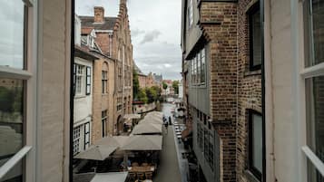 Una calle estrecha flanqueada por edificios, con mesas al aire libre y sombrillas, y un canal en el centro.