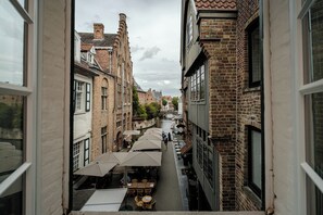 A narrow street with buildings on either side, outdoor seating with umbrellas, and a canal in the center. - Hotel Bourgoensch Hof (Bruges)