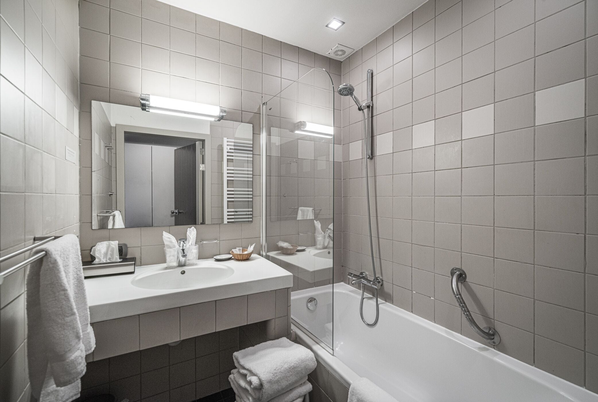 A modern bathroom with a large mirror, two sinks, a bathtub, and a glass-enclosed shower.