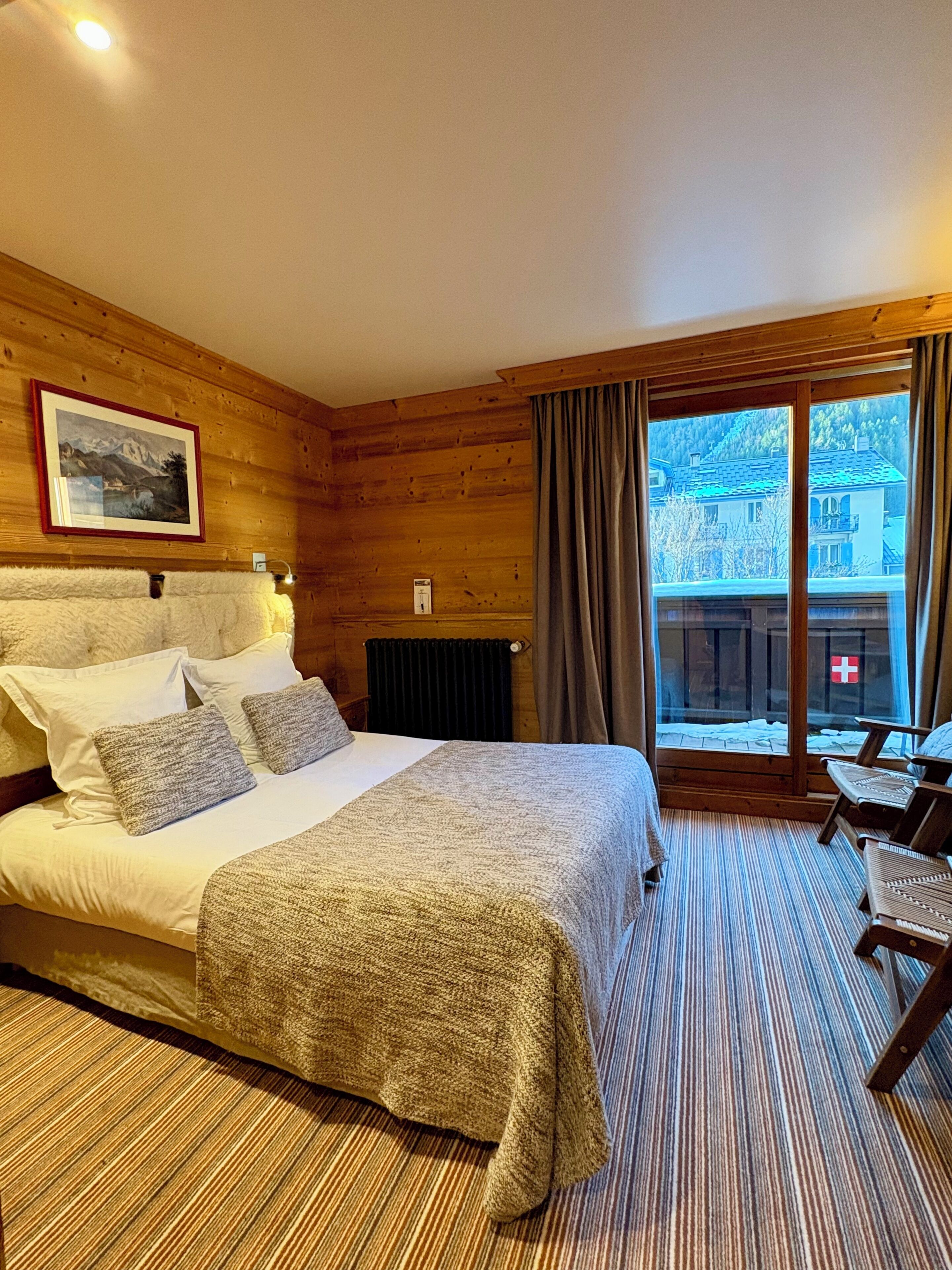 A hotel room with a bed, a chair, a window with curtains, and a wooden wall.
