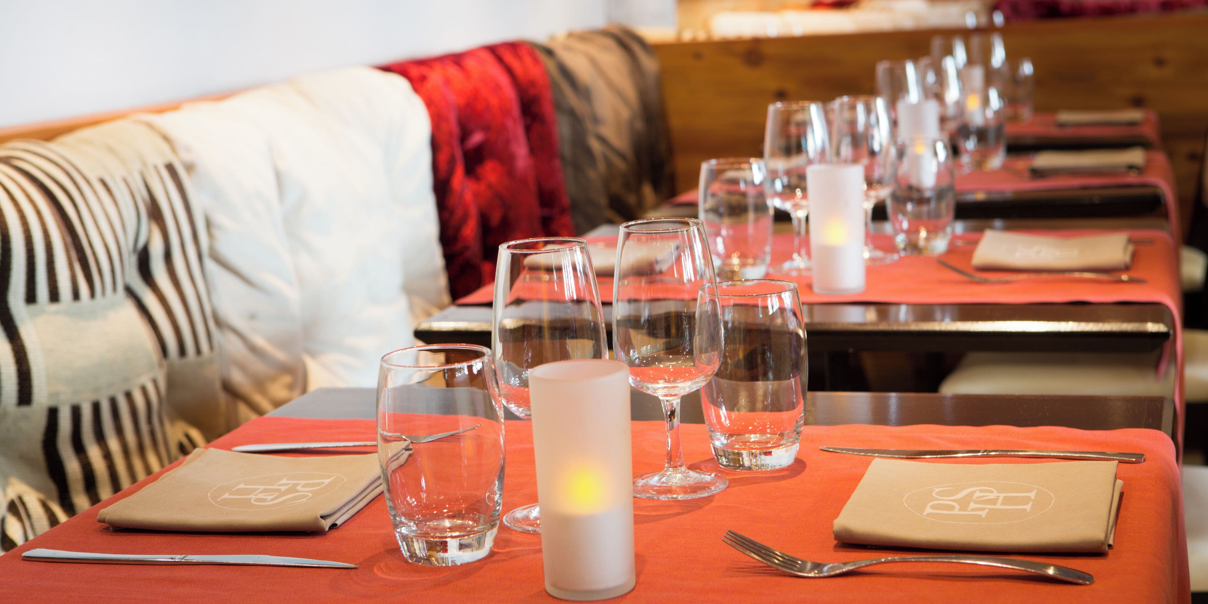 Ein Restaurantambiente mit gedeckten Tischen, darunter klares Glas und Servietten mit einem Logo.