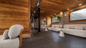 Un interior moderno con paneles de madera, un sofá, una silla y vistas a montañas.
