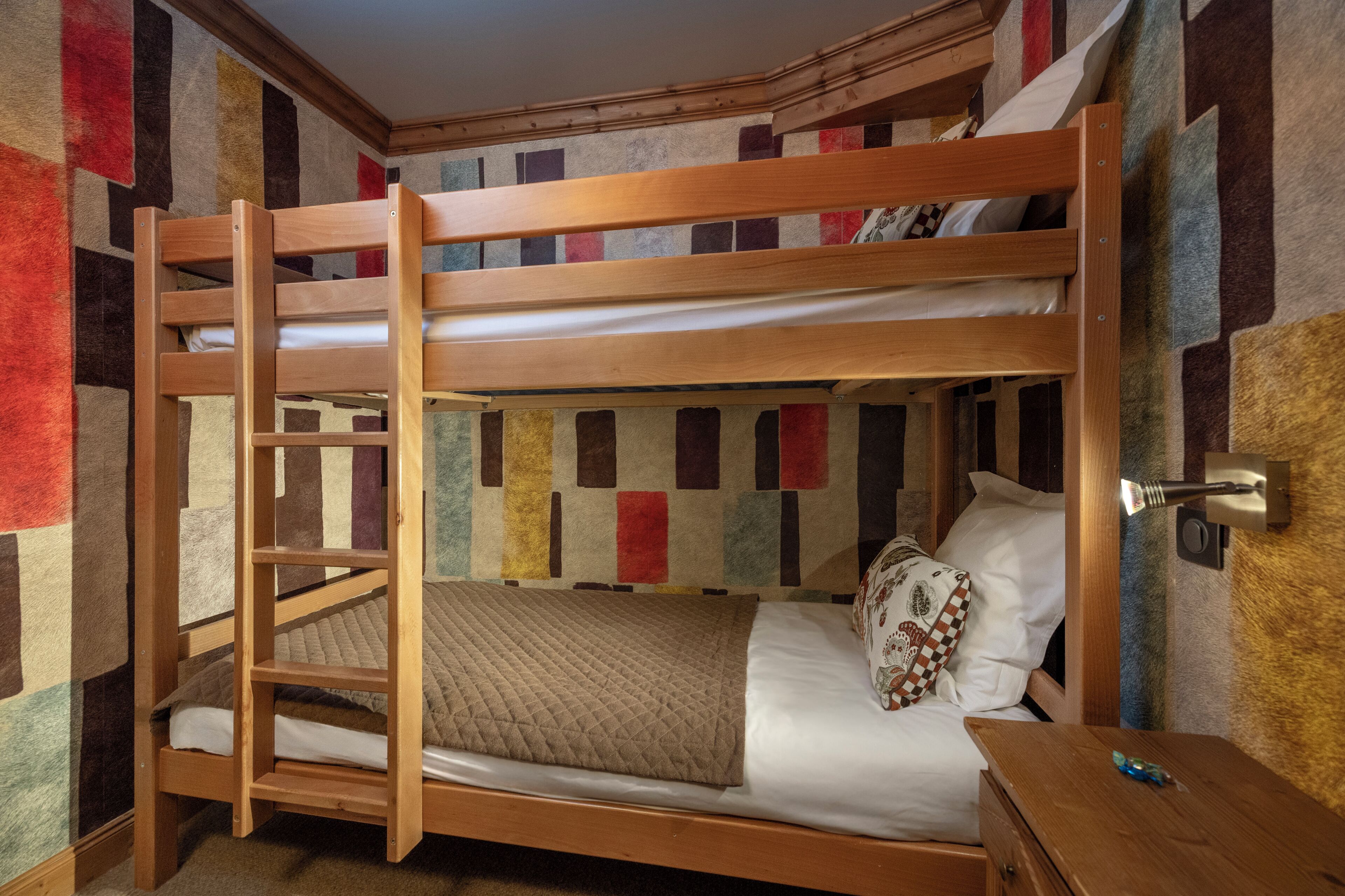 Un lit superposé avec une échelle, une couverture matelassée et un oreiller à motifs à carreaux.