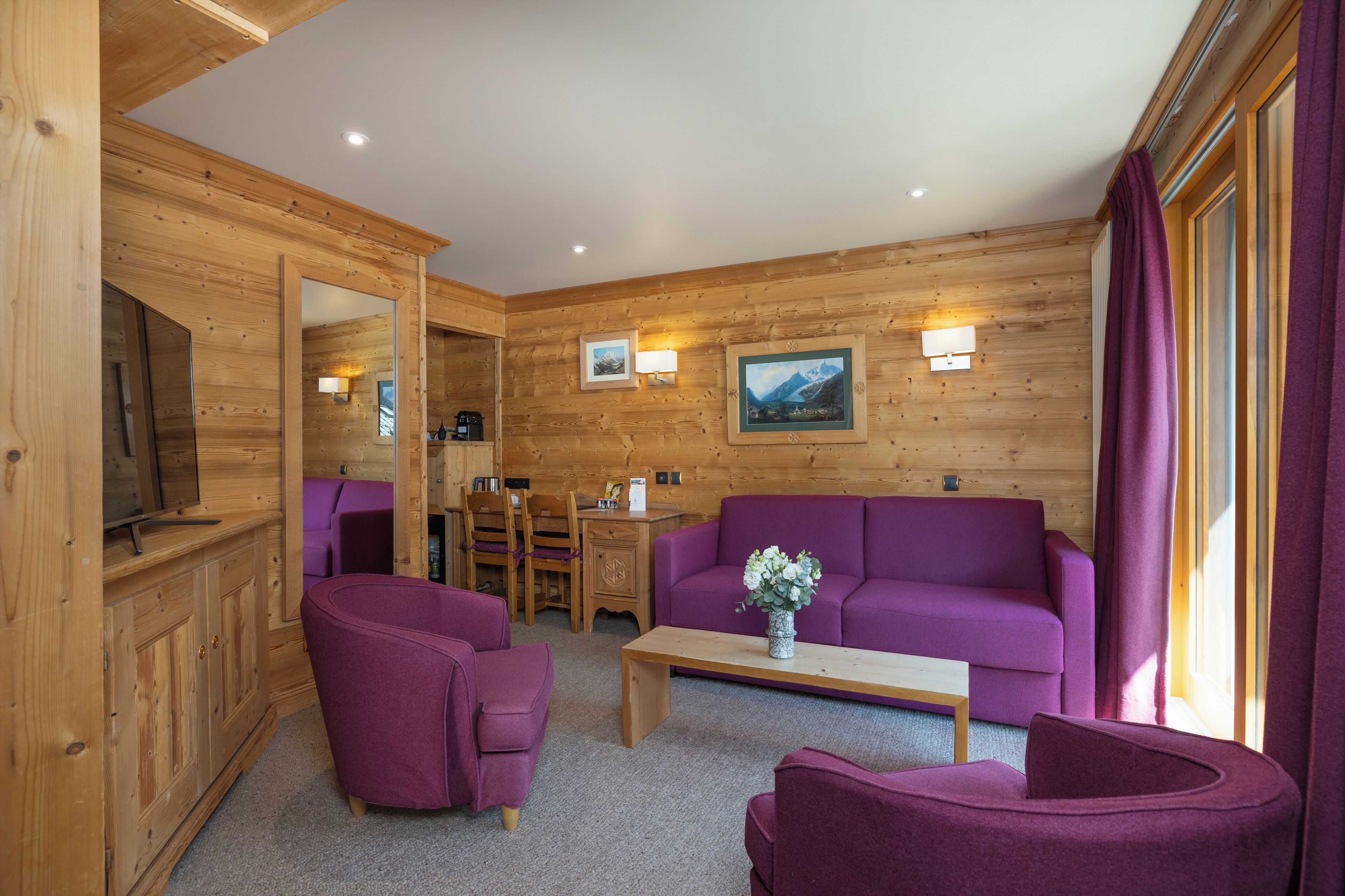 A wooden interior with a purple sofa, a coffee table, and a TV.