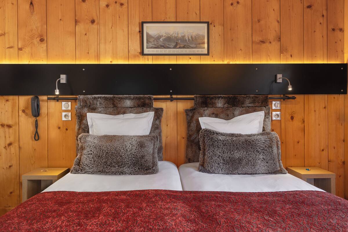 Ein Doppelbett mit roter Decke, zwei Nachttische mit Lampen, ein gerahmtes Bild an der Wand und Holzvertäfelung.