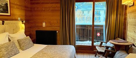A hotel room with a bed, a small table, and a view of the outside.