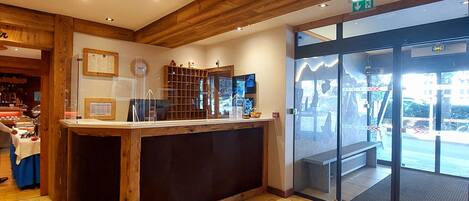 Un área de recepción con mostrador de madera, puerta de vidrio que da al exterior y un emblema circular en el suelo.