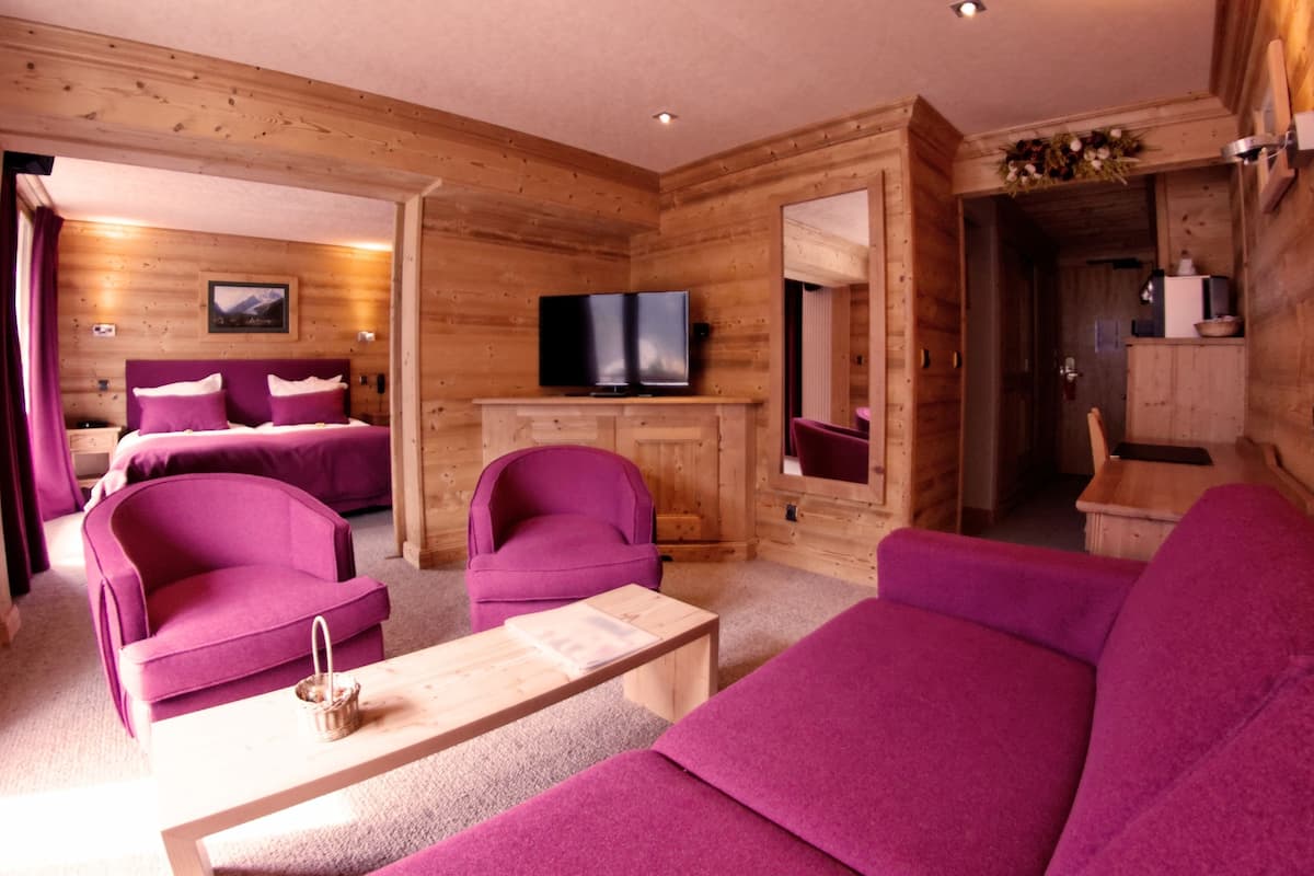 Ein Interieur einer Blockhütte mit einem Wohnbereich, der violette Möbel, einen Fernseher und einen Kamin zeigt.