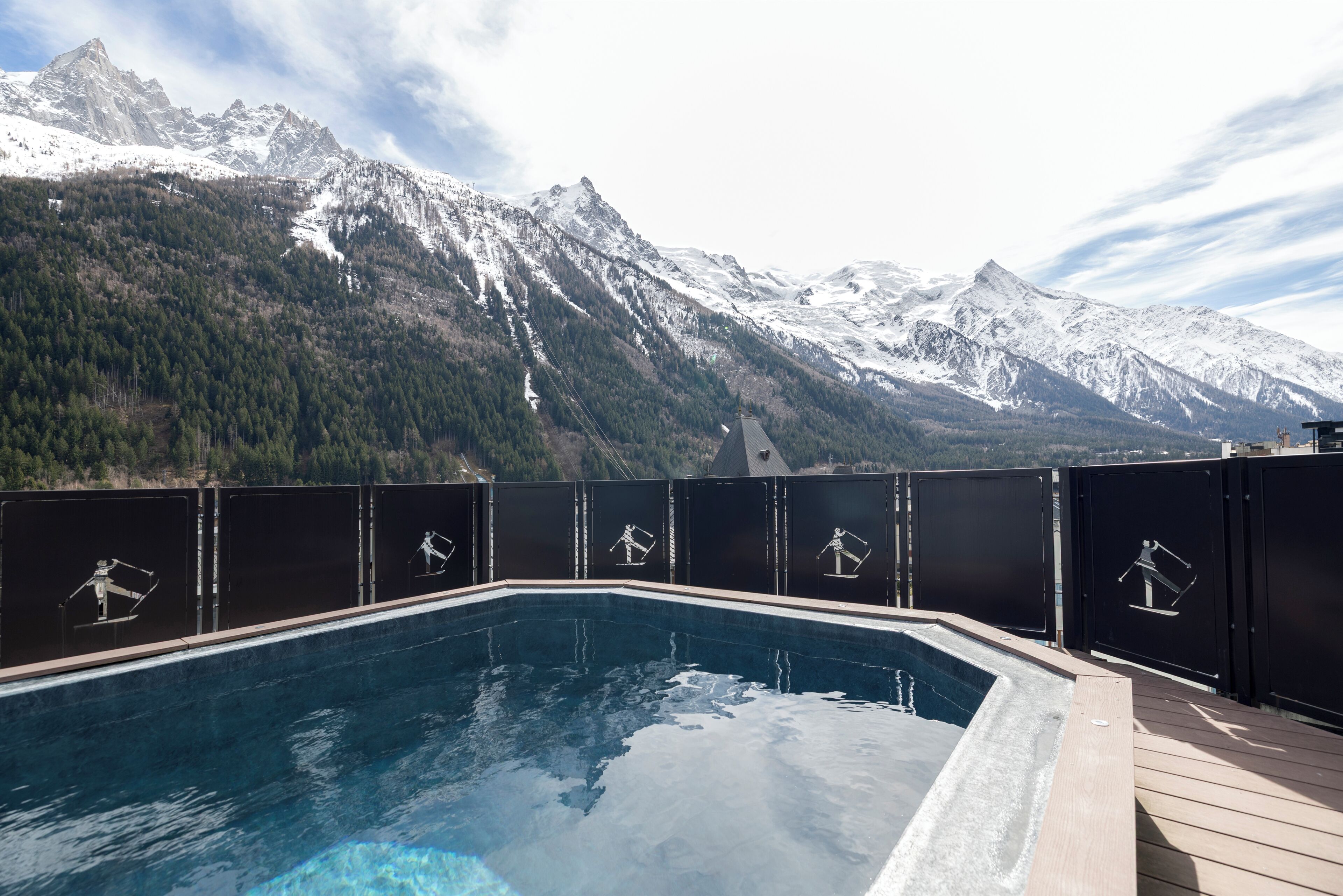 Une piscine avec vue sur les montagnes, entourée d’une terrasse et d’une clôture ornée de motifs décoratifs.