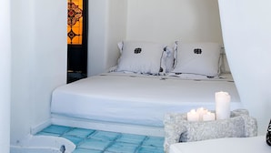 A modern, minimalist room with a white bed, a small seating area, and a unique blue-tiled floor. - Blue Angel Villa (Santorini)