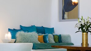 A room with a tiled floor, a sofa with teal cushions, a vase with flowers, and a wall-mounted light fixture. - Blue Angel Villa (Santorini)