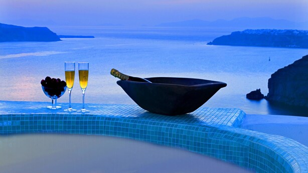 A pool with a view of the sea, two glasses of champagne, and a bowl. - Blue Angel Villa (Santorini)