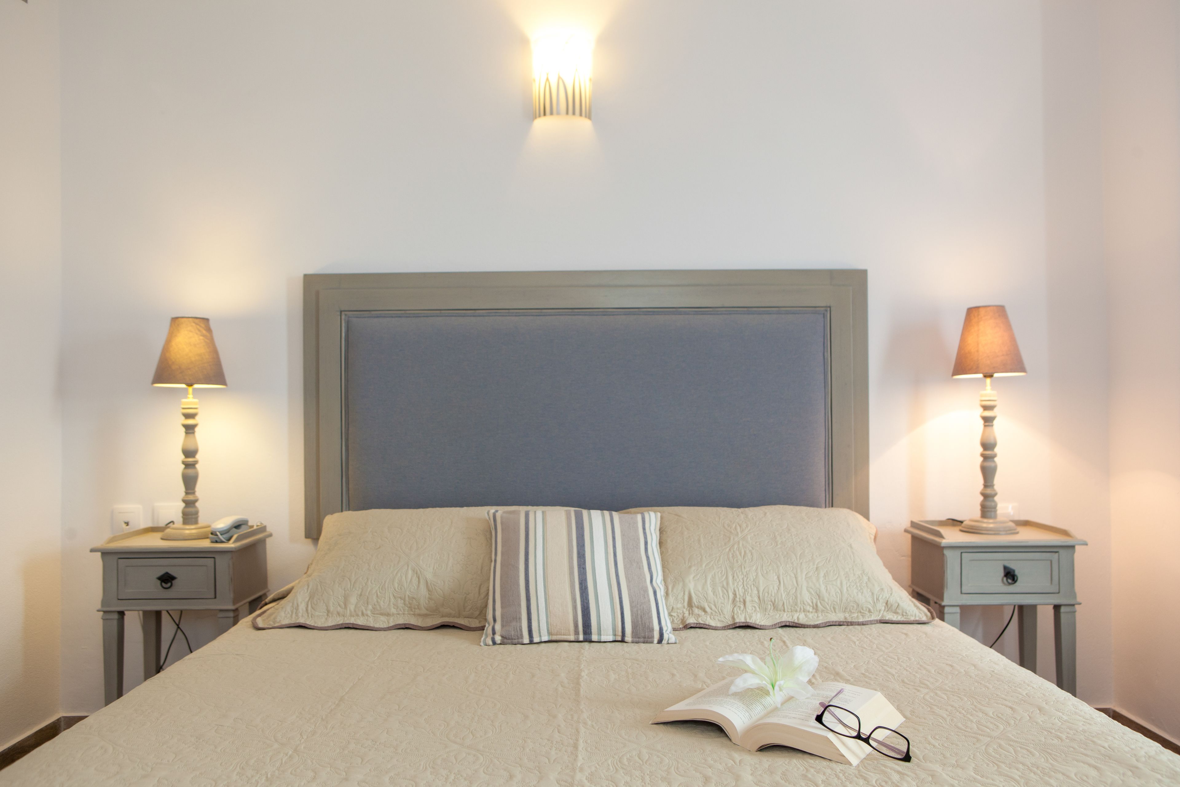 A neatly made bed with a striped pillow, two bedside tables with lamps, and a wall-mounted light fixture.