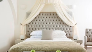 Un dormitorio con cabecera capitonada, cama con dosel, dos mesitas de noche con lámparas y una silla.
