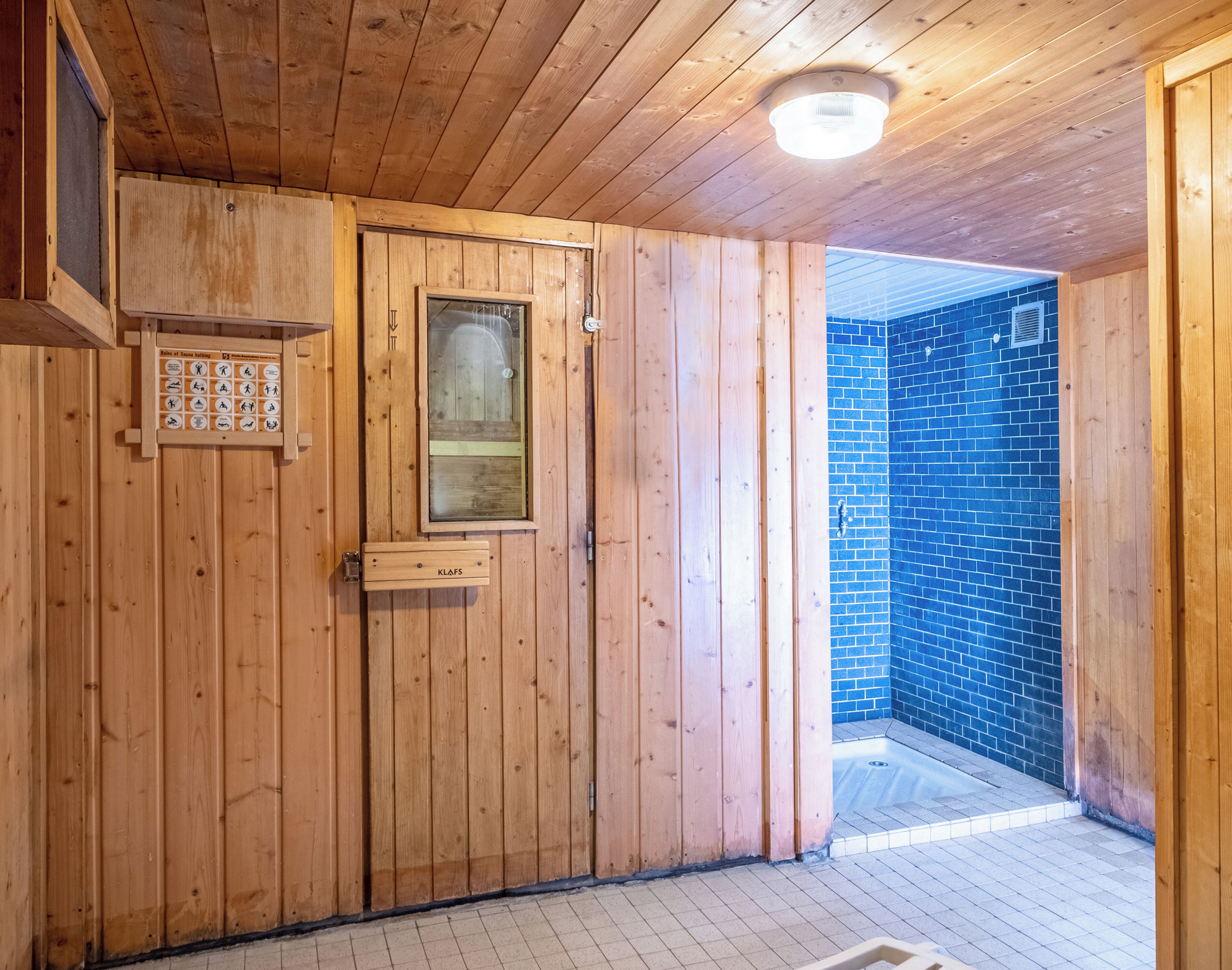 Interior de madera con una puerta de sauna, una ventana y una pared con azulejos azules.
