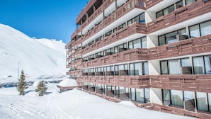 A multi-story hotel with balconies, large windows, and a snowy mountain backdrop.