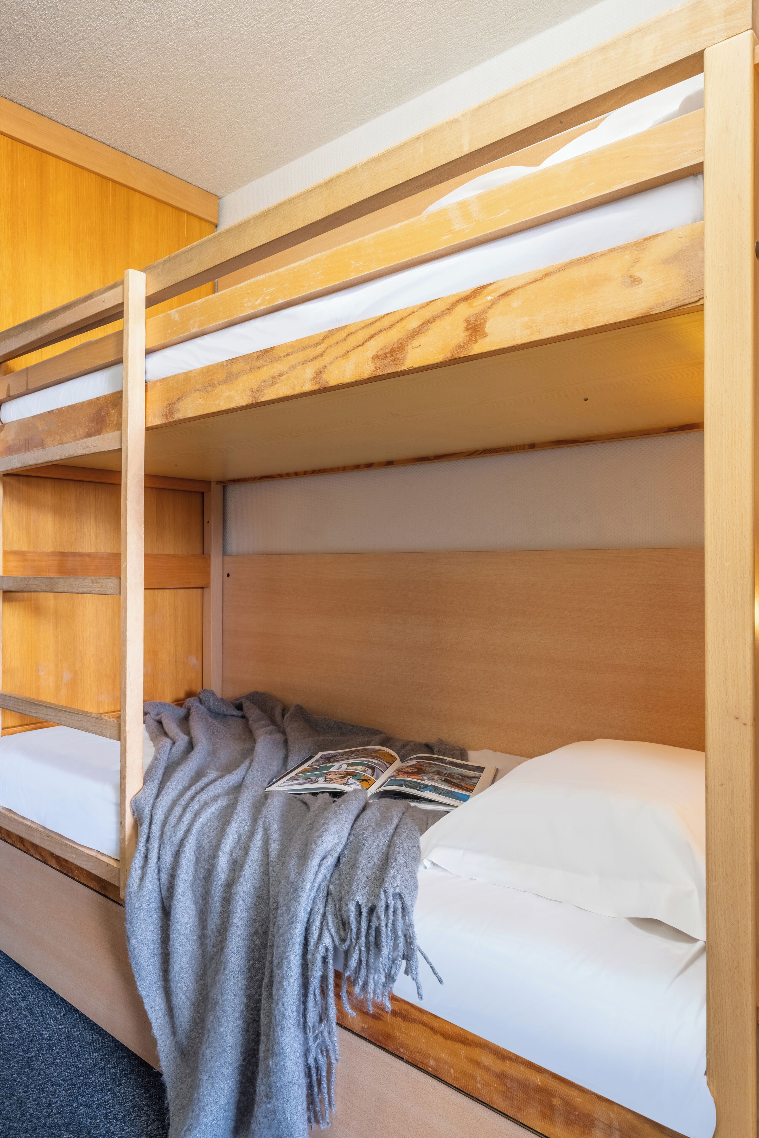A bunk bed with a wooden headboard, a grey blanket, and a magazine on the lower bunk.