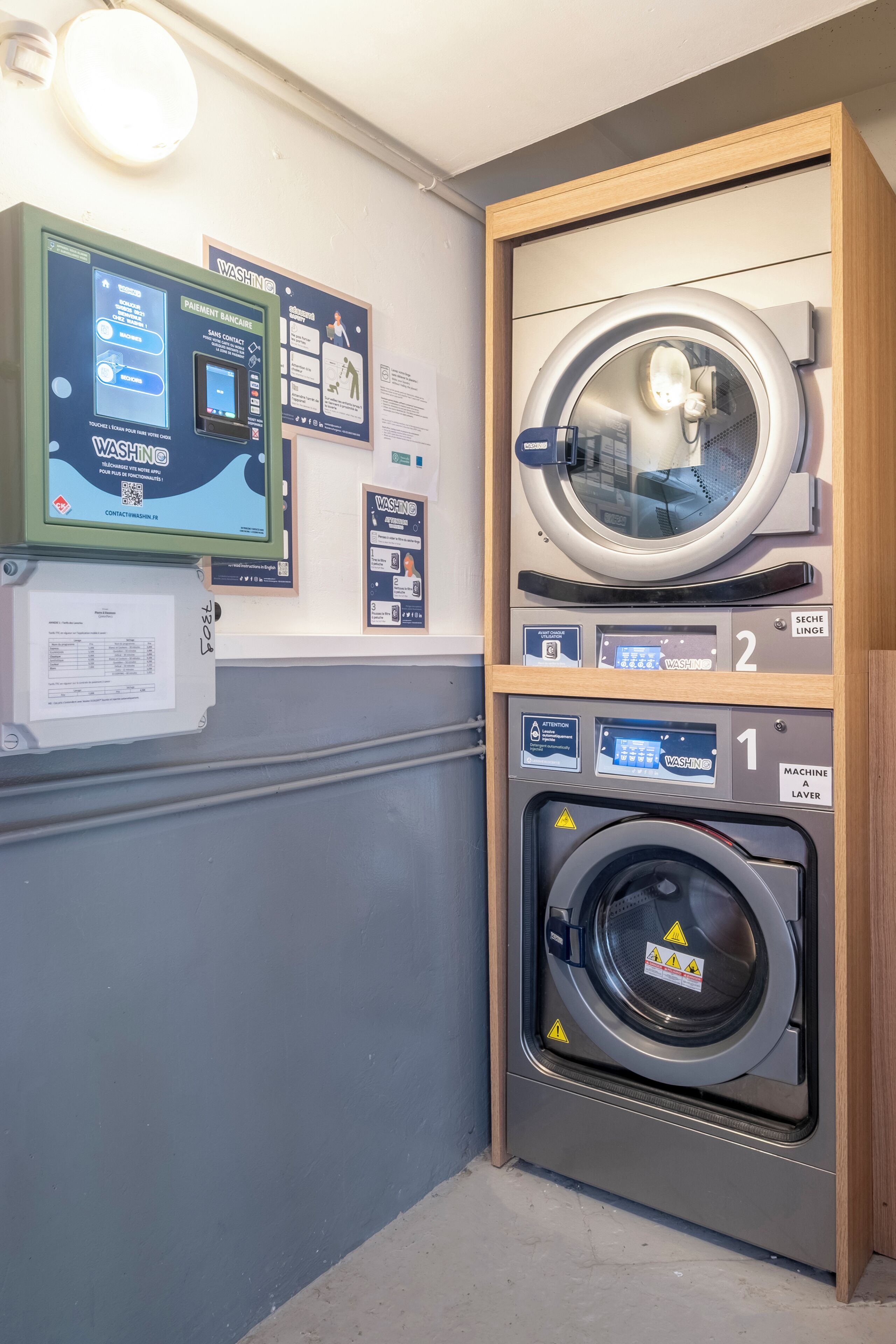 A public laundromat with a washing machine, dryer, and a payment kiosk.
