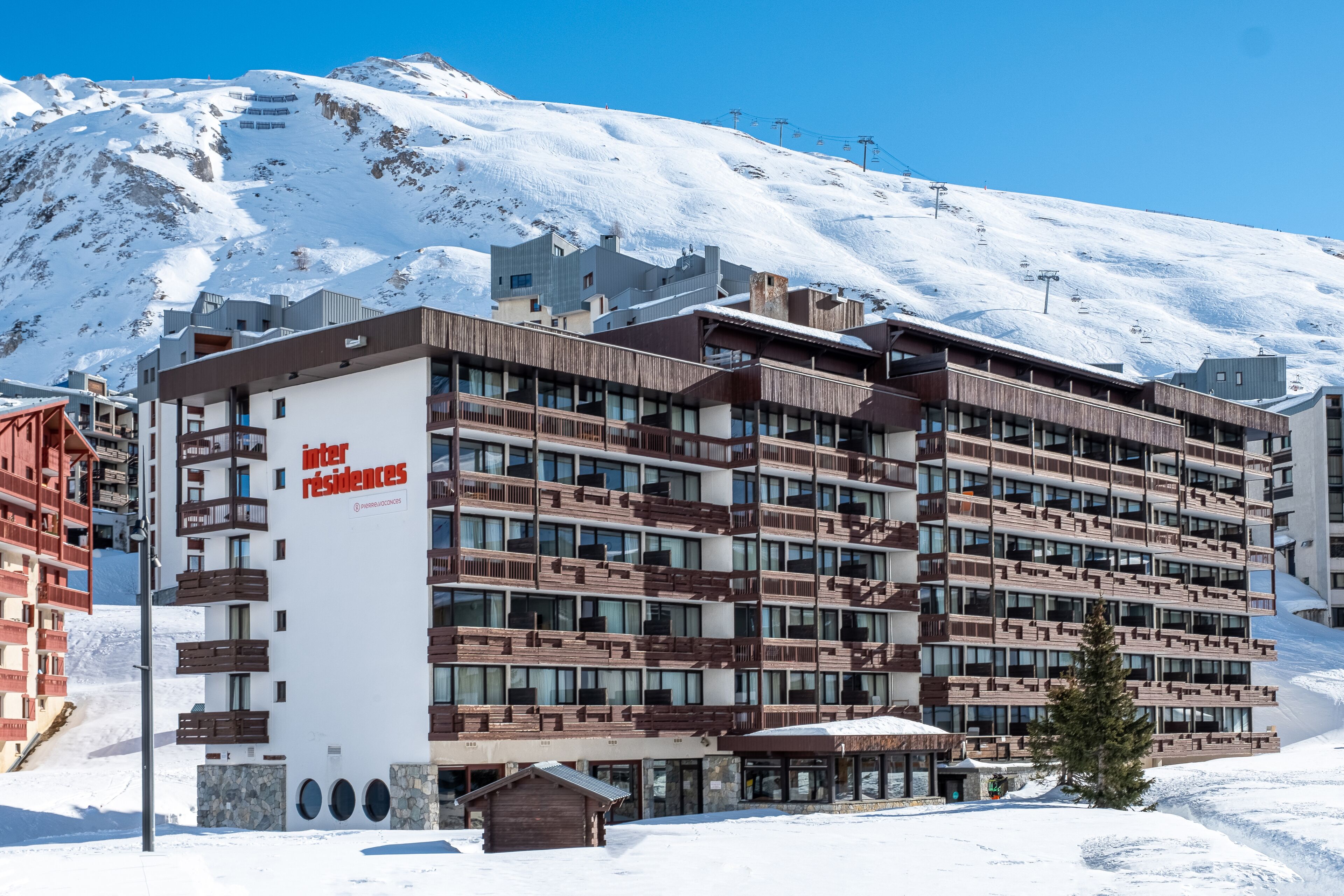 A multi-story hotel with a modern design, featuring balconies and large windows, situated in a snowy mountainous area.