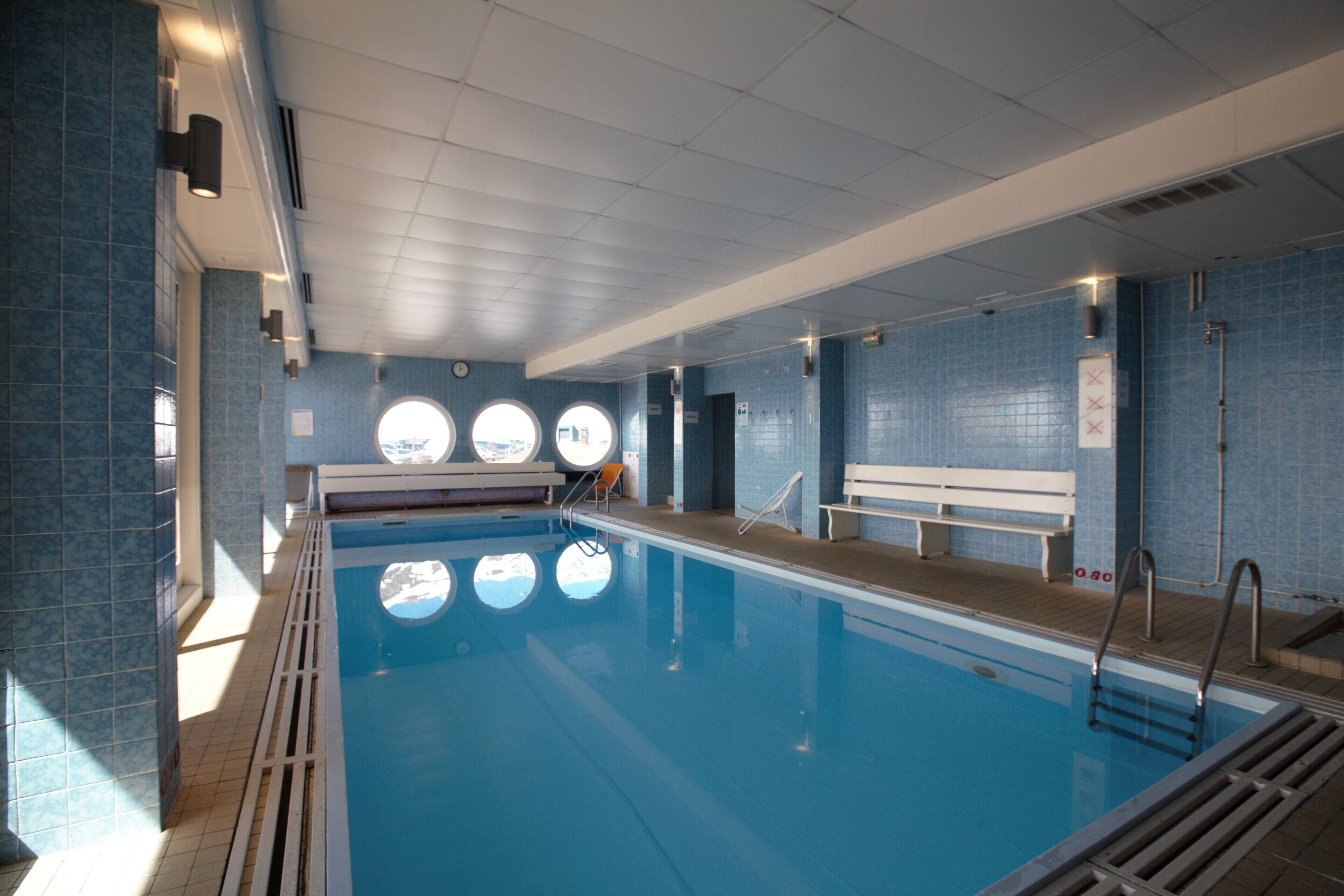 An indoor swimming pool with clear blue water, tiled walls, and a bench along the side.