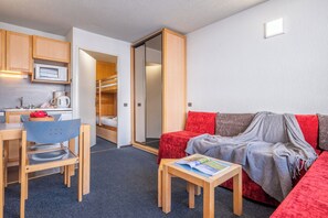 A compact room with a kitchenette, a dining area, a sofa, and a small table with a magazine.