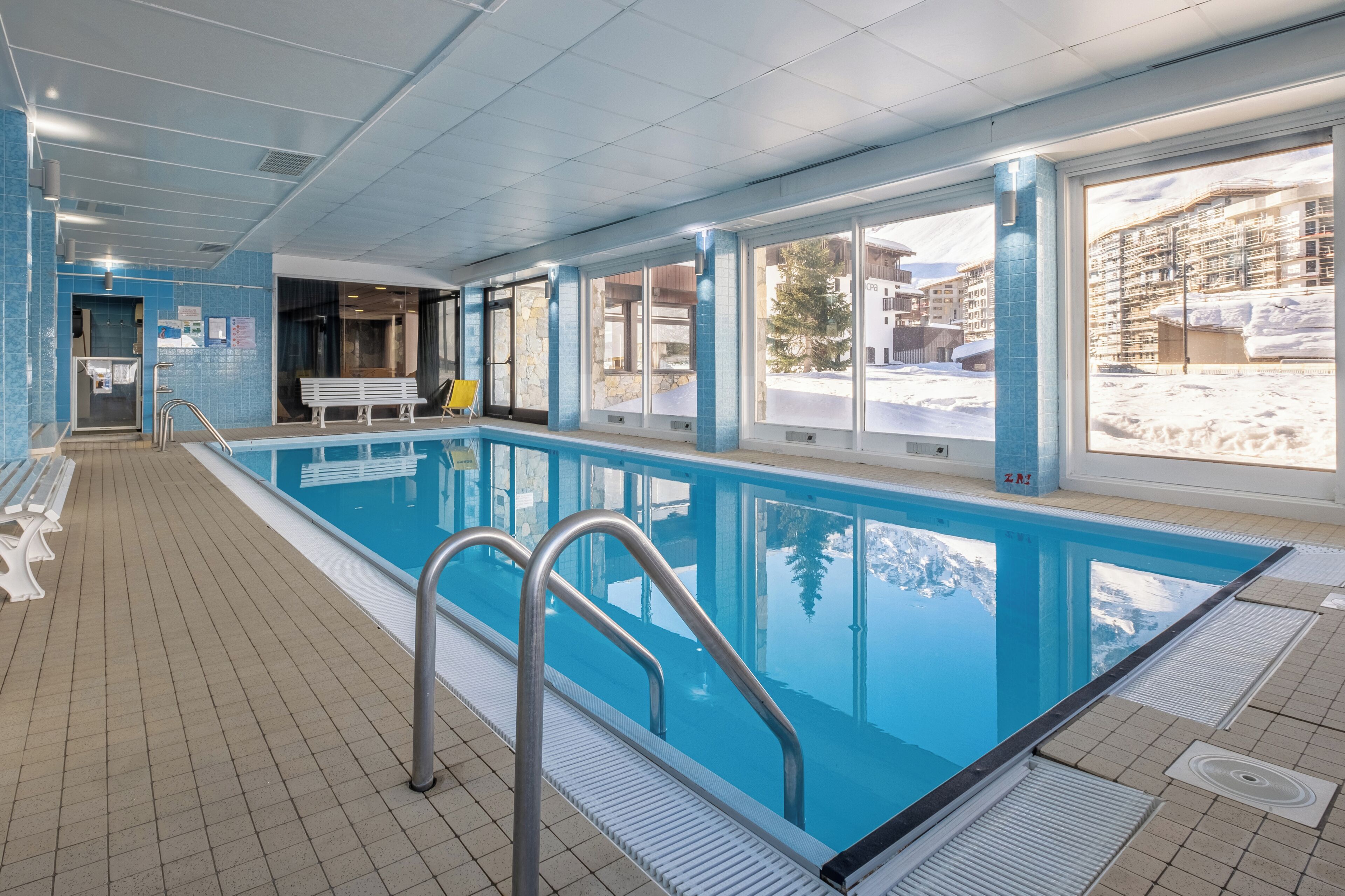 Une piscine intérieure avec de grandes baies vitrées, un sol carrelé et un banc.