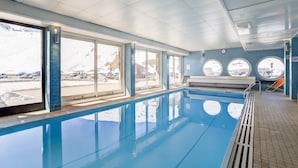 An indoor swimming pool with large windows, a tiled floor, and a view of a snowy landscape.