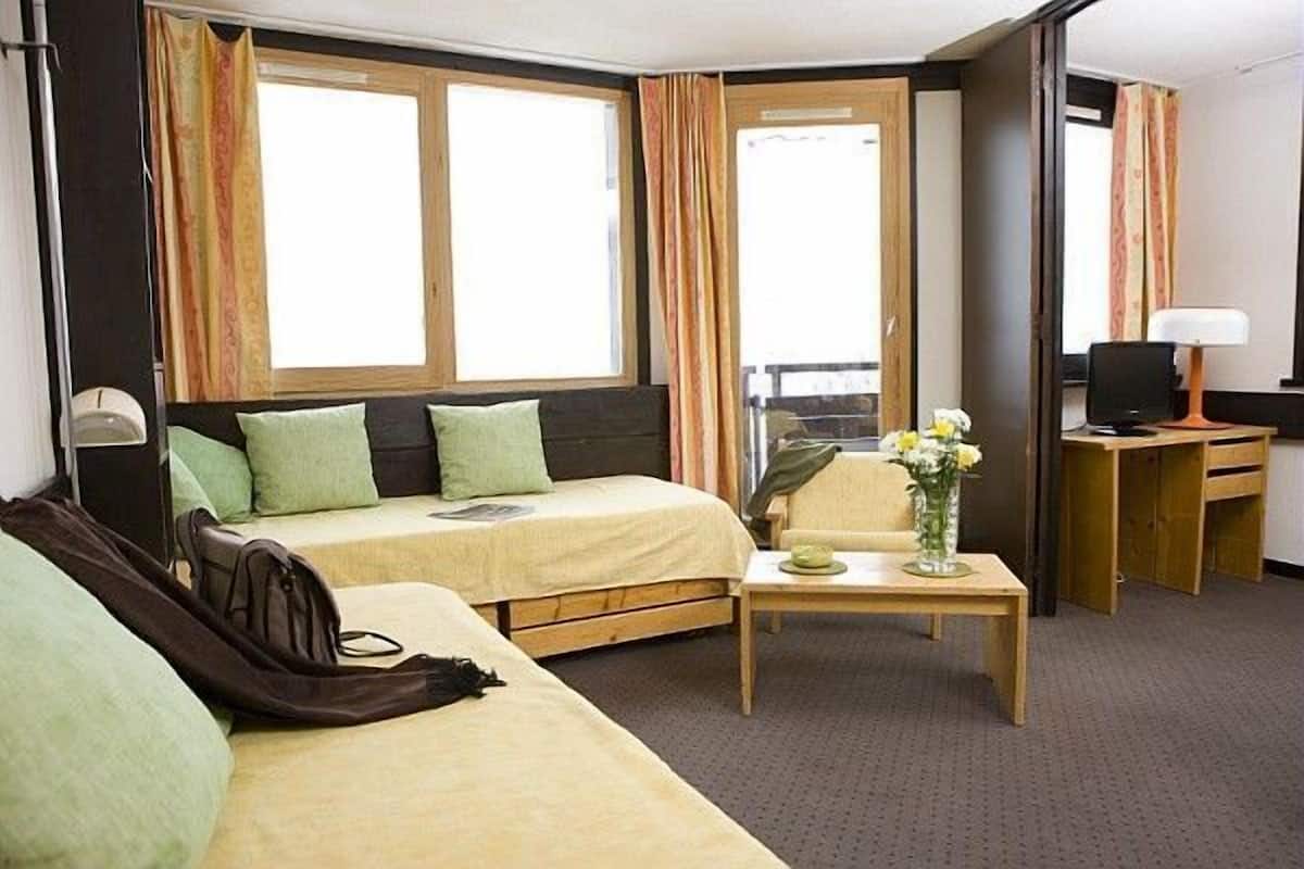Habitación de hotel con cama, escritorio, silla, mesita con un florero y televisor.