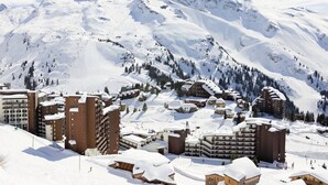 Uma cidade nas montanhas coberta de neve, com vários edifícios, incluindo hotéis e casas, e uma pista de esqui ao fundo.