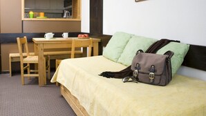 Quarto compacto com uma cama, escrivaninha e cadeira. Possui uma pequena área de cozinha com pia e prateleira com utensílios.