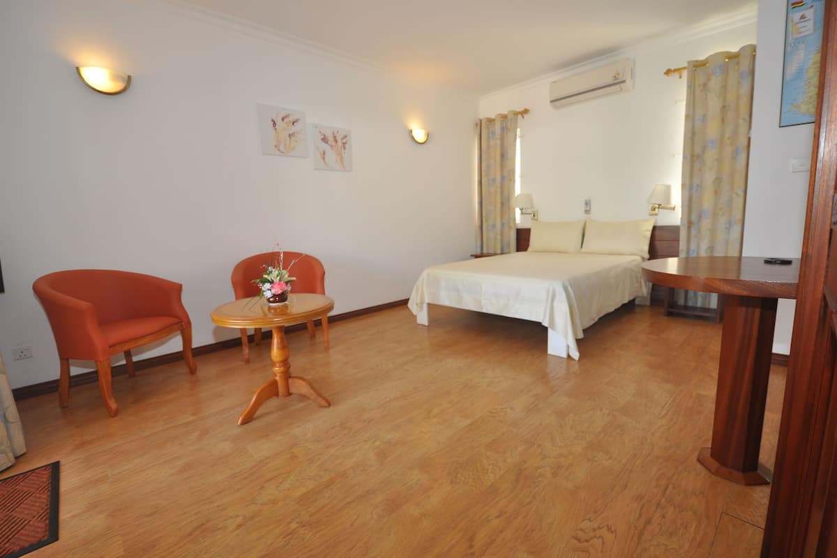 A hotel room with a bed, a small round table with a vase of flowers, a red armchair, and a wooden side table.