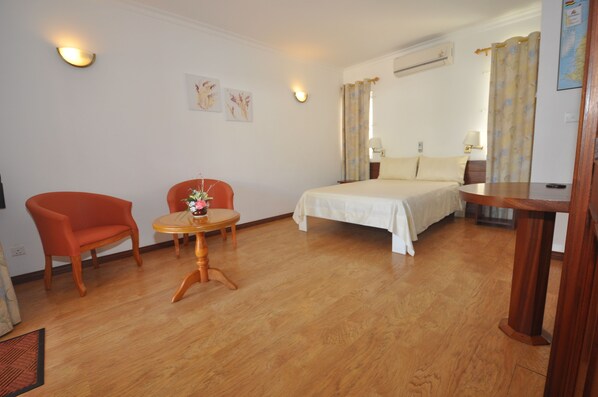 A hotel room with a bed, a small round table with a vase of flowers, a red armchair, and a wooden side table.