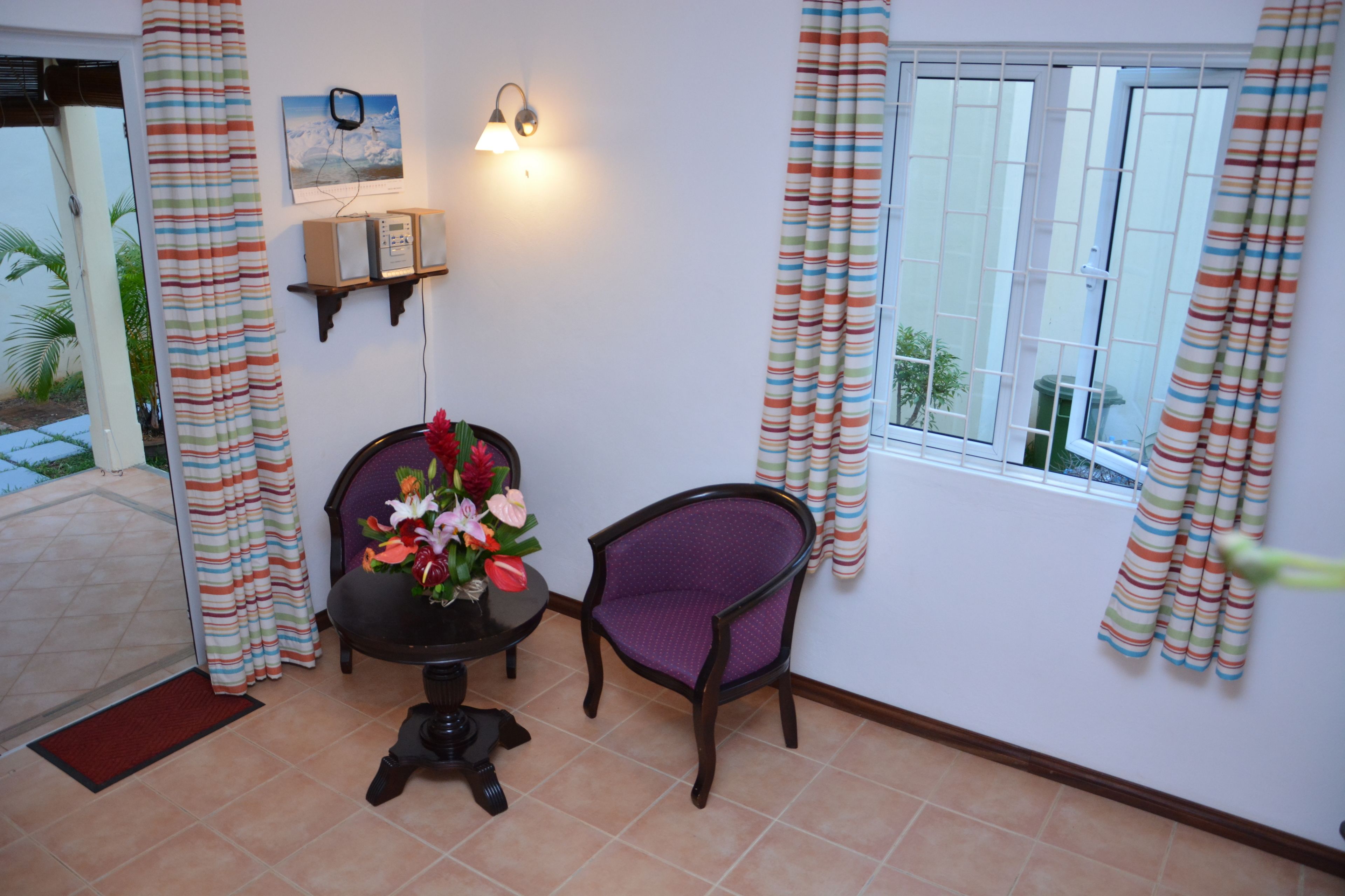 A room with a dining table, two chairs, a wall-mounted light fixture, and a window with curtains.