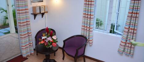 A room with a dining table, two chairs, a wall-mounted light fixture, and a window with curtains.