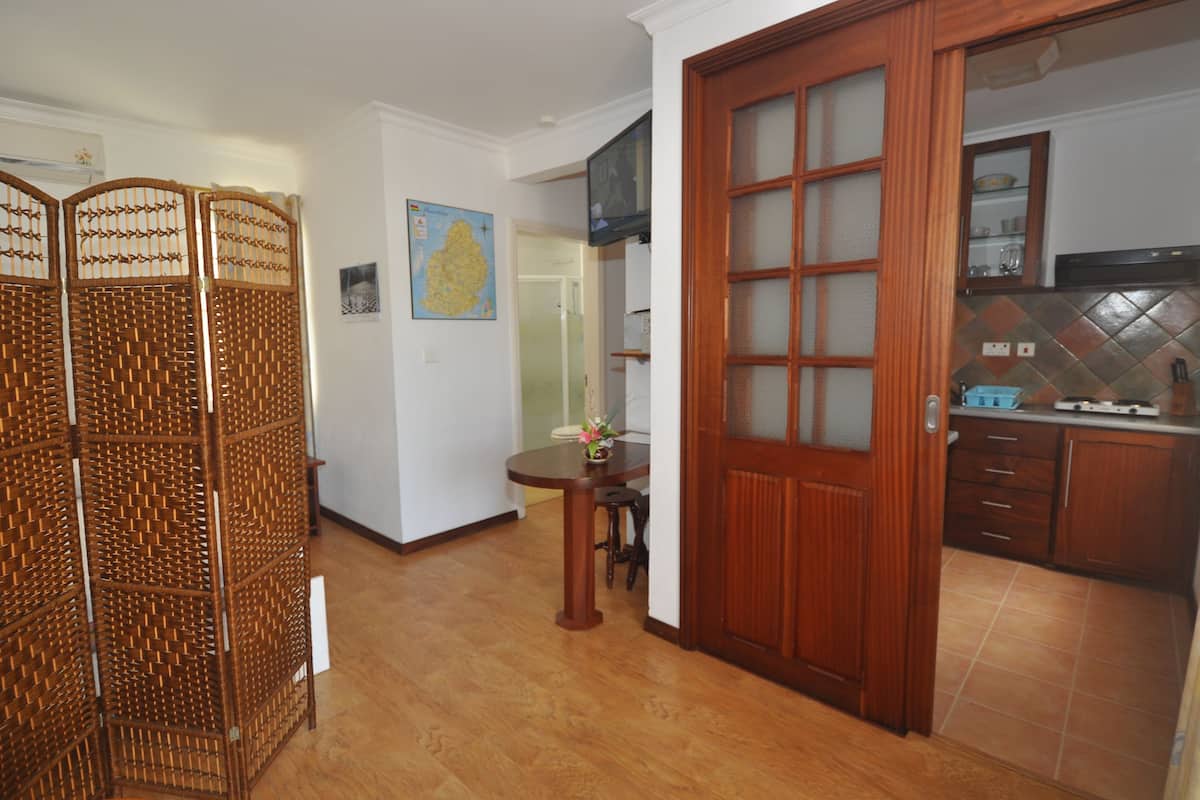 A room with a wooden floor, a dining table with chairs, a kitchen area with cabinets and a stove, and a wooden door with glass panels.