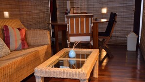 A room with a wicker sofa, a glass-top coffee table, and a wooden chair. - La Pointe Villas (Grand-Baie)