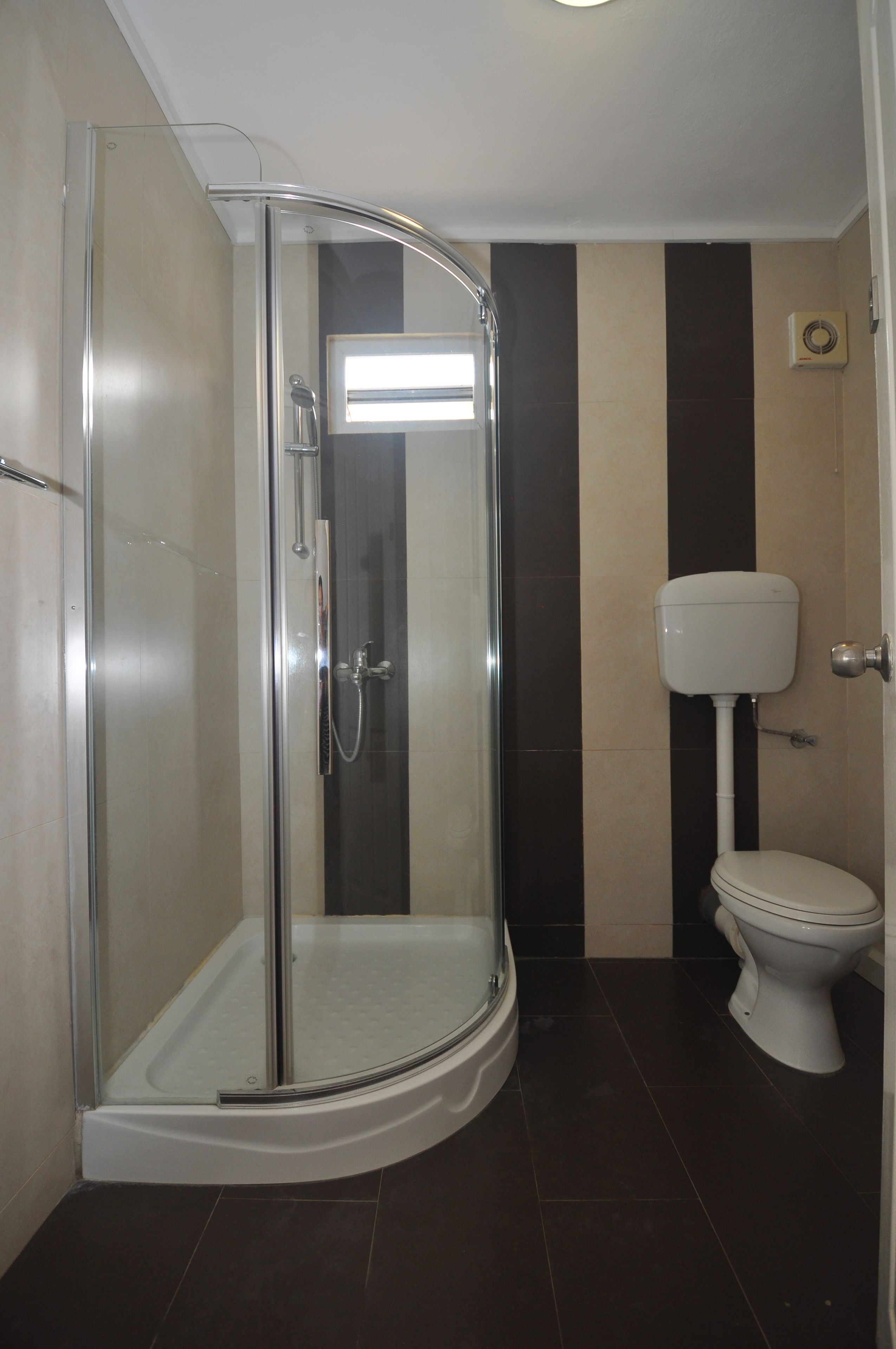 A modern bathroom with a glass-enclosed shower, a toilet, and a wall-mounted air conditioning unit.