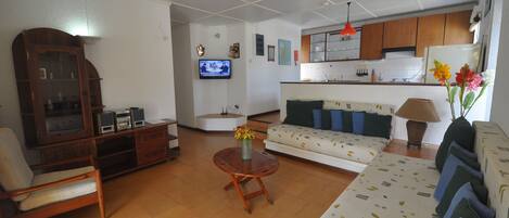 A living room with a sofa, armchair, wooden cabinet, and a television.