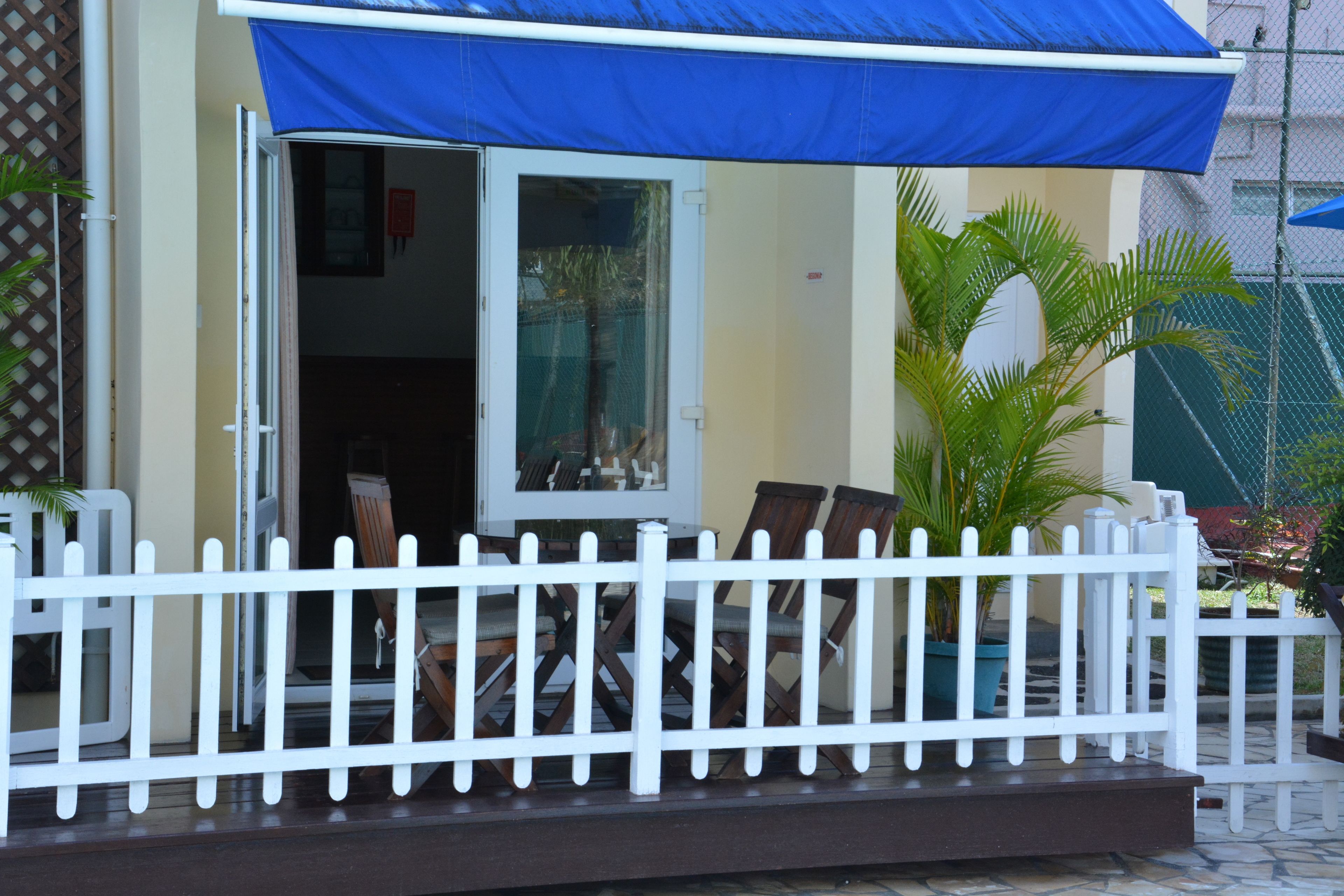 A covered outdoor seating area with a white picket fence, a table, and chairs.