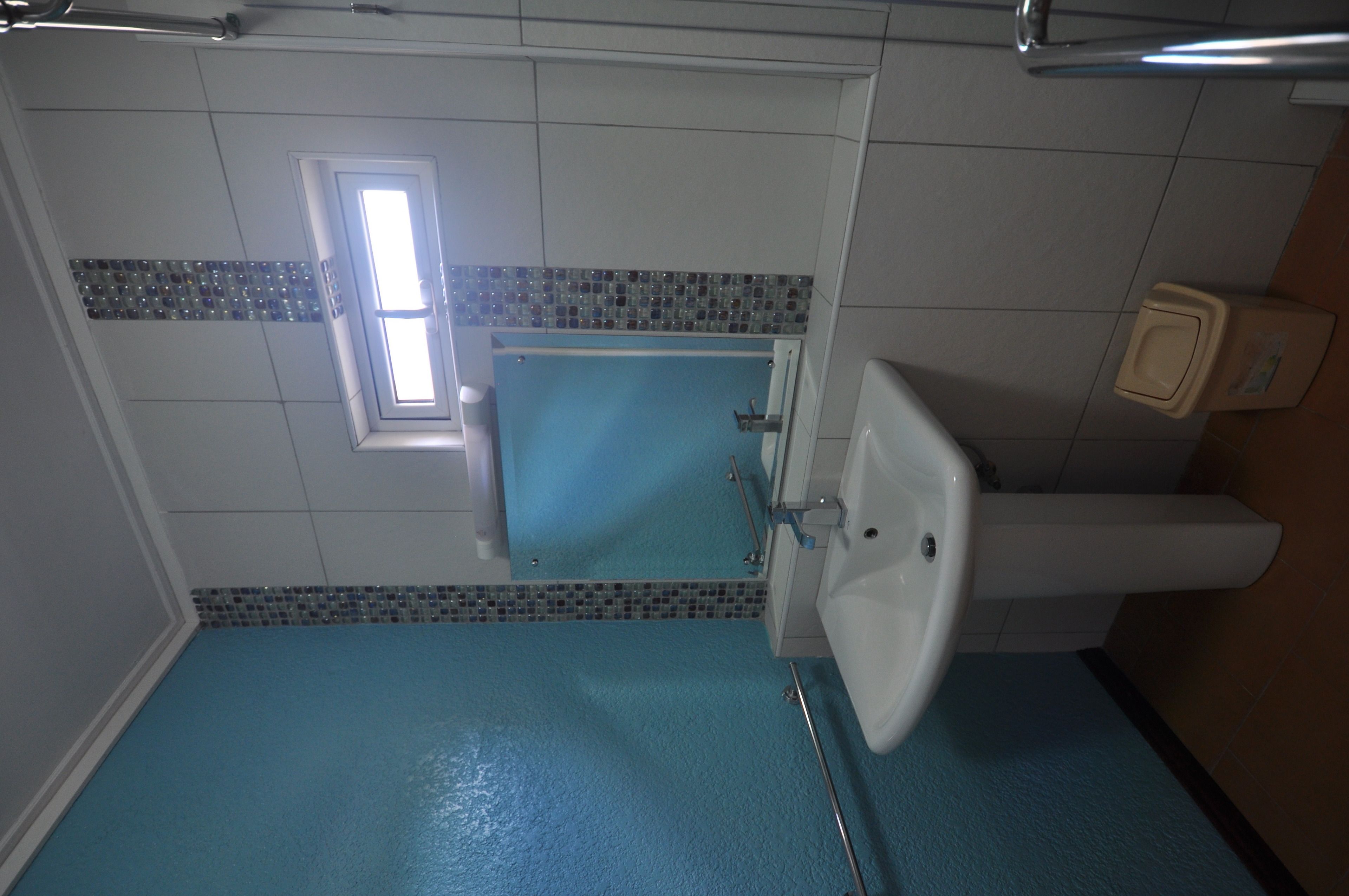 Une salle de bain avec un sol bleu, un lavabo blanc et un miroir.
