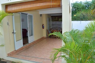 Un patio techado con puerta corrediza de vidrio que da a una habitación, una mesa con sillas y un extintor colgado en la pared.