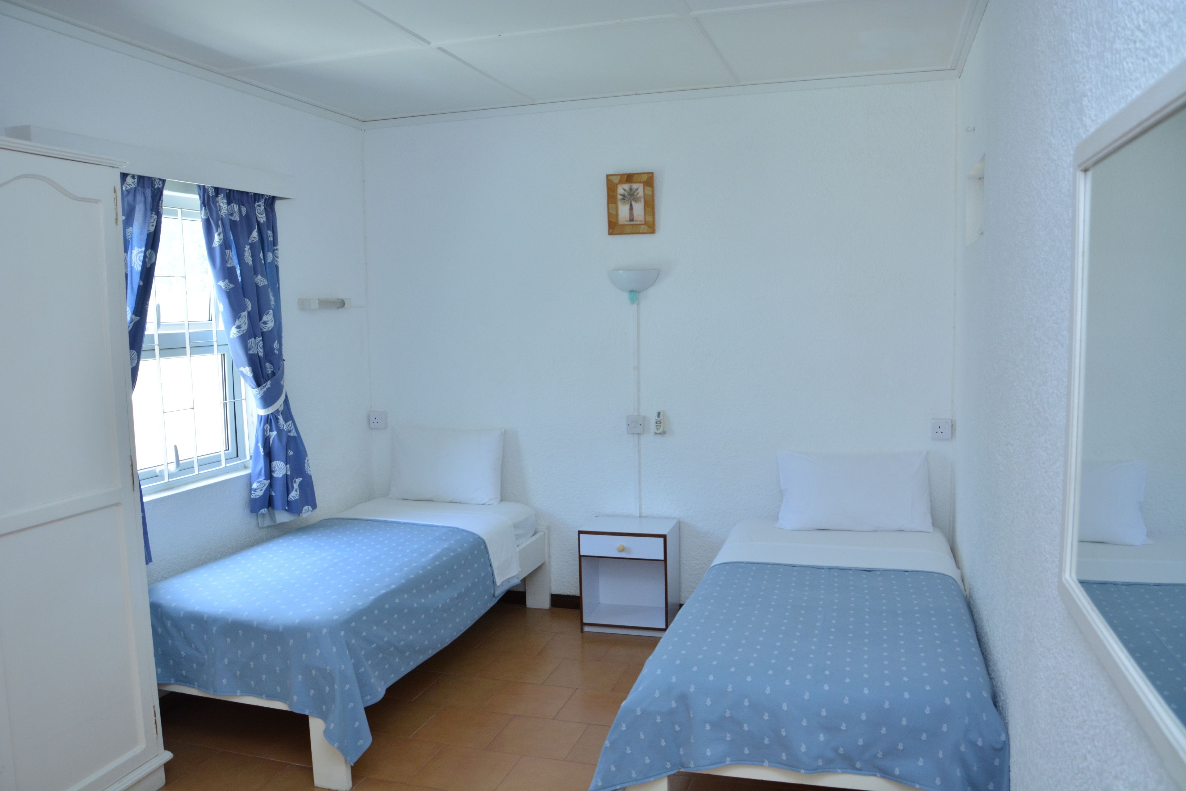 A room with two single beds, a nightstand, a lamp, and a window with curtains.
