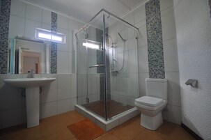 Un baño con ducha de mampara de vidrio, lavamanos pedestal y retrete.